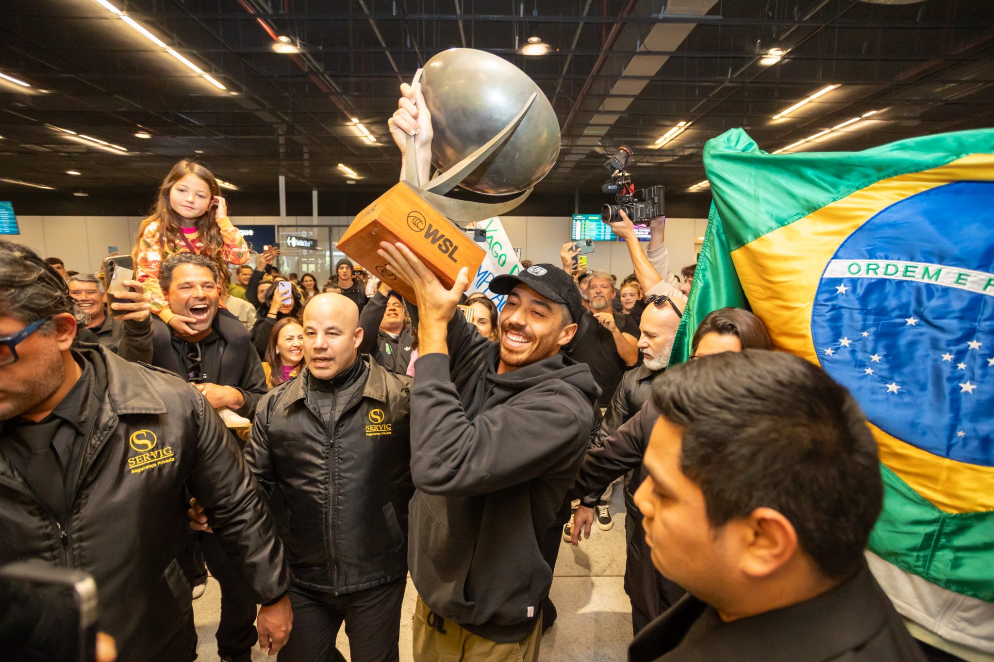 2025 WSL world chanpion Yago Dora arrives at Florianopolis airport to a large crowd, carrying the large trophy.